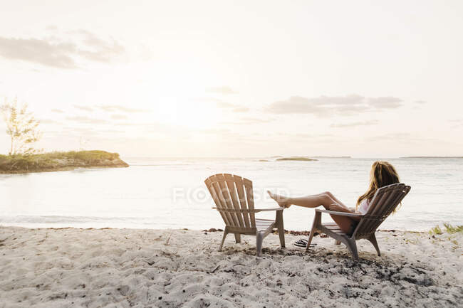 Junge Frau sitzt am Strand bei Sonnenuntergang auf den Bahamas — Stockfoto