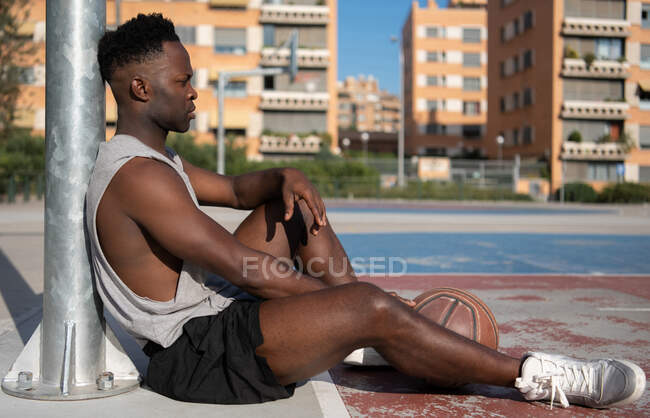 Exhausted African American man resting near pole on basketball court on street — Stock Photo