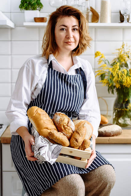 Jovencita sosteniendo pan en la cocina - foto de stock
