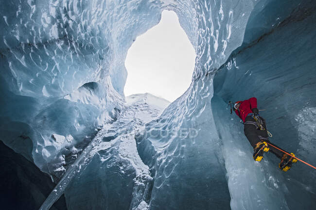 Человек карабкается на сосульку в ледниковой пещере Исландии — стоковое фото
