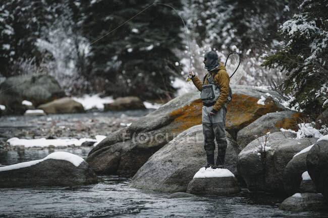 Mann beim Fliegenfischen im Winter auf Felsen stehend — Stockfoto