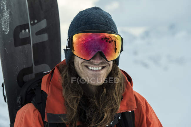 Porträt eines lächelnden Mannes in warmer Kleidung, der im Urlaub Snowboard trägt — Stockfoto