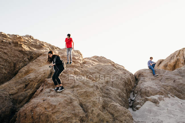Братья и сёстры на пляже забираются на большие скалы — стоковое фото
