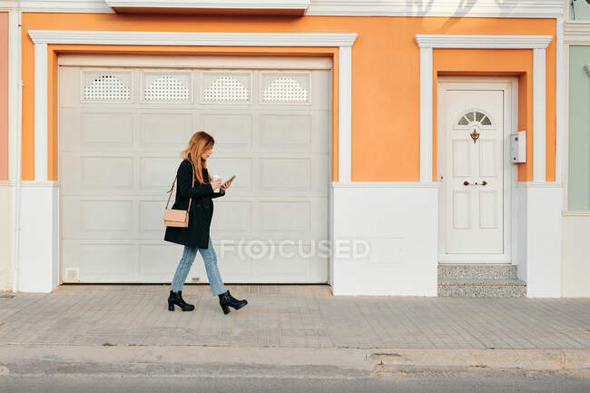 Mulher andando enquanto ela olha para seu smartphone na rua — Fotografia de Stock