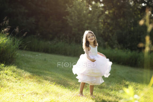 Dulce niña en vestido blanco girando y bailando en un prado. - foto de stock