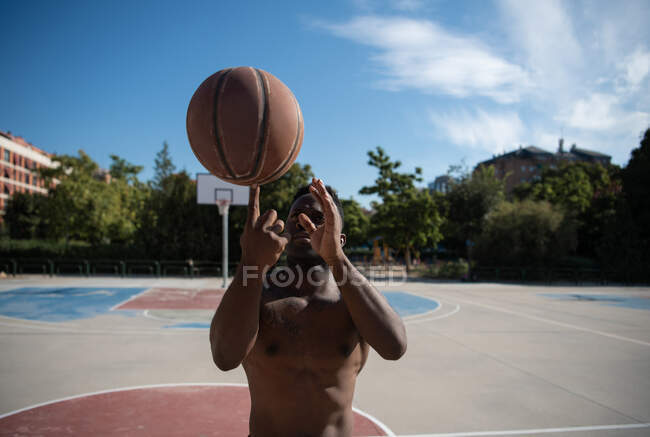 М'язистий чорний чоловік робить трюк з баскетбольним м'ячем під час тренувань у сонячний день — стокове фото