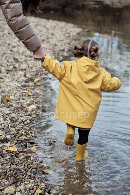 Uma menina de 2 anos com a mãe na margem de um rio — Fotografia de Stock