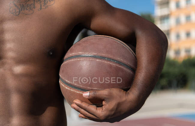 Cultivado atleta muscular afroamericano con pelota de pie en la cancha de baloncesto - foto de stock