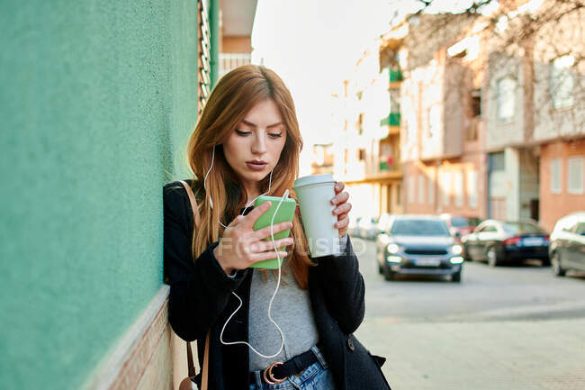 Femme d'affaires tenant une tasse de café tandis qu'elle regarde son téléphone en écoutant de la musique sur un fond vert — Photo de stock