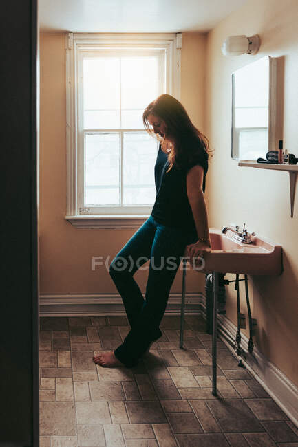 Attractive woman leaning against a pink sink in an old bathroom. — Stock Photo