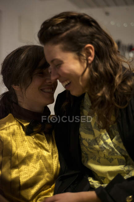Queer lesbian couple laugh at home in kitchen armchair at dinner party — Stock Photo