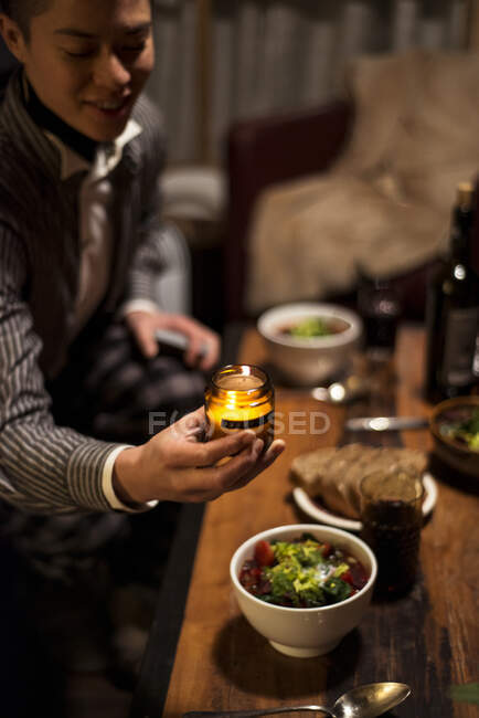 Queer person smiles and places candle at dinner table at night — Stock Photo