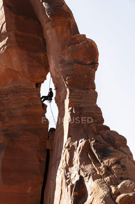 Vista de bajo ángulo del hombre escalando en formaciones rocosas contra el cielo despejado en el Parque Nacional Canyonlands - foto de stock