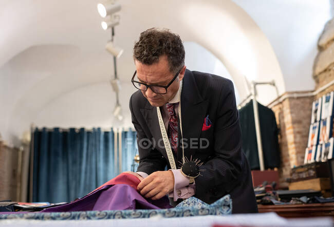 Focado homem maduro comparando e escolhendo tecidos durante o trabalho no estúdio loft — Fotografia de Stock
