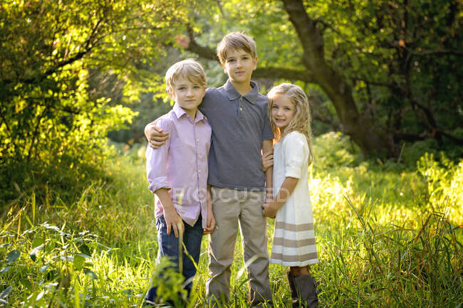 Drei liebevolle blonde Kinder stehen zusammen auf einer Wiese. — Stockfoto