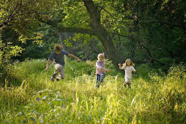 Tres niños rubios corriendo en un hermoso campo. - foto de stock