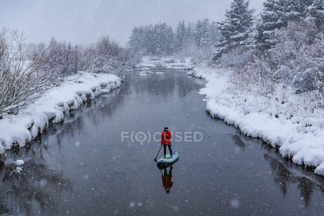 Woman doing stand up paddleboarding on river during winter — Stock Photo