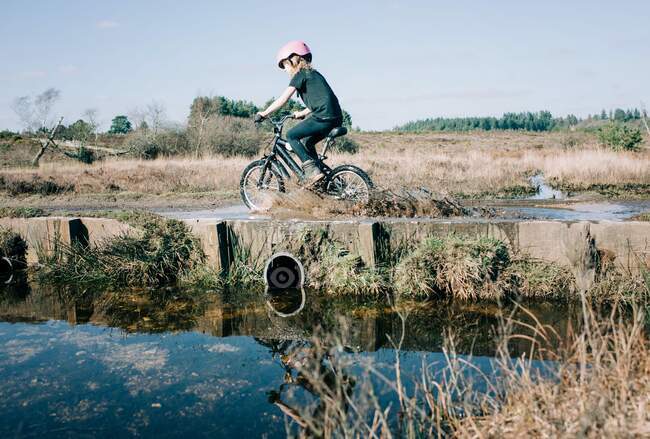 Jovem menina em sua bicicleta equitação através de um grande poça salpicando — Fotografia de Stock
