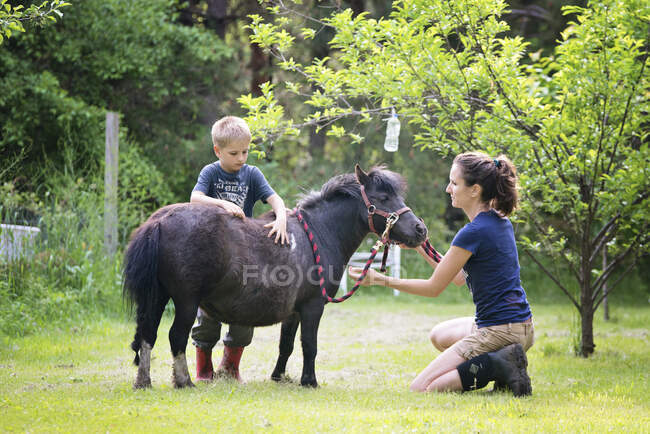 Madre y niño pequeño con un pony negro. - foto de stock