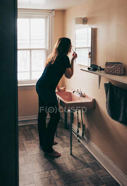 Женщина опирается на розовую раковину в старой ванной комнате, чтобы нанести макияж. — стоковое фото