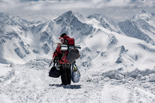 Вид сзади на мужчину-туриста с сумками во время прогулки по заснеженной горе во время отпуска — стоковое фото