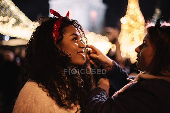 Happy young woman standing with girlfriend in city during Christmas — Stock Photo