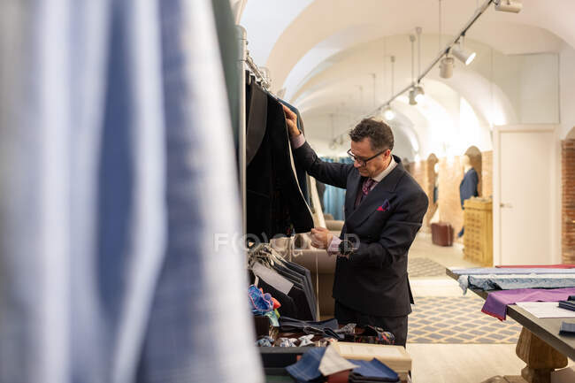 Sastre masculino maduro usando cinta adhesiva para medir la manga de una chaqueta elegante en atelier - foto de stock