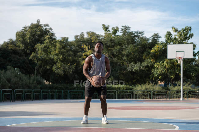 Focused ethnic man with basketball throw preparing to score on sports ground — Fotografia de Stock