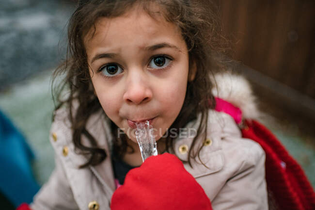Happy preschool girl eating icicle with mittens — Stock Photo