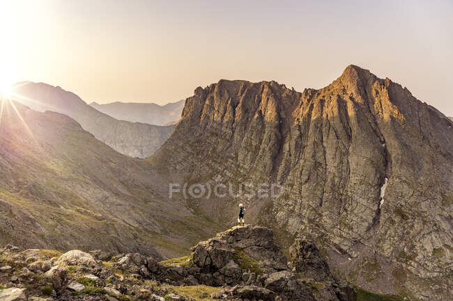 Mujer mirando a la vista mientras está de pie en el pico de la montaña contra el cielo despejado durante el atardecer - foto de stock