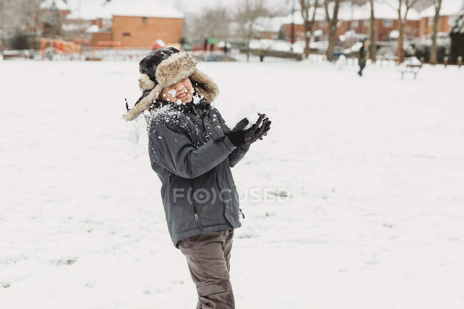Menino sendo atingido na cara por bola de neve com casas cobertas de neve atrás — Fotografia de Stock