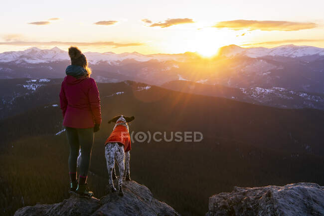 Mulher com cão olhando para a paisagem do pico da montanha durante o pôr do sol — Fotografia de Stock