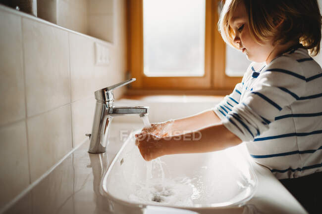 Vista lateral de niños pequeños en edad preescolar lavándose las manos con jabón - foto de stock