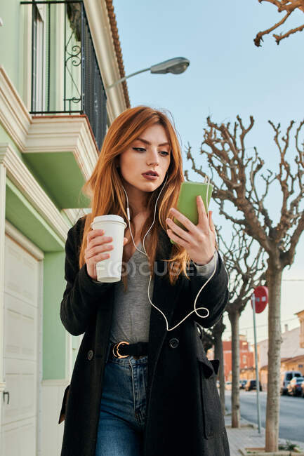 Mujer caminando mientras mira su teléfono inteligente en la calle - foto de stock