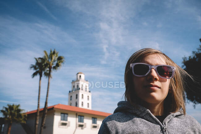 Niño con gafas de sol se para frente a las palmeras y la torre - foto de stock