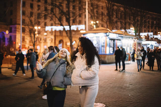 Glückliche Freundinnen, die im Winter nachts auf der Straße in der Stadt spazieren gehen — Stockfoto