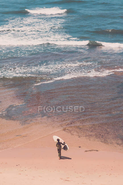 Ragazzo che cammina verso l'oceano portando la tavola da surf. — Foto stock