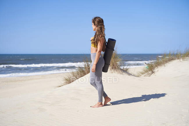 Junges und freies Mädchen, das nach Beendigung ihrer Yoga-Stunde am Strand auf den Ozean blickt. Konzept von Freiheit, Frieden und gesundem Leben. — Stockfoto