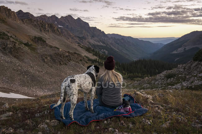 Femme regardant les montagnes en randonnée avec chien pendant le coucher du soleil — Photo de stock