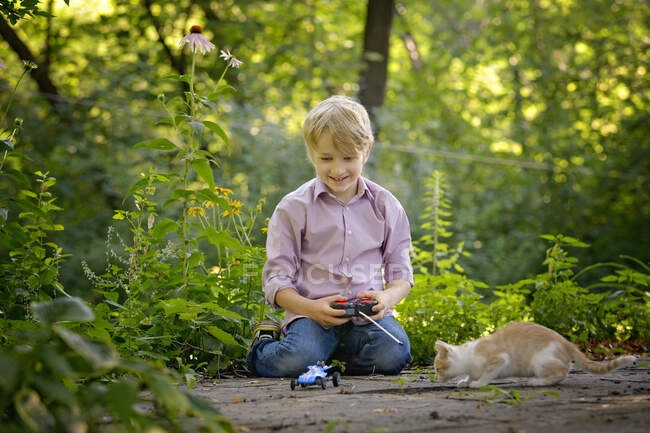 Pequeño niño rubio jugando con el gatito y el coche de control remoto. - foto de stock