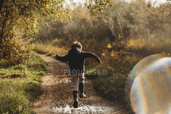 Visão traseira do menino pulando sobre poça enlameada no caminho lateral do canal — Fotografia de Stock