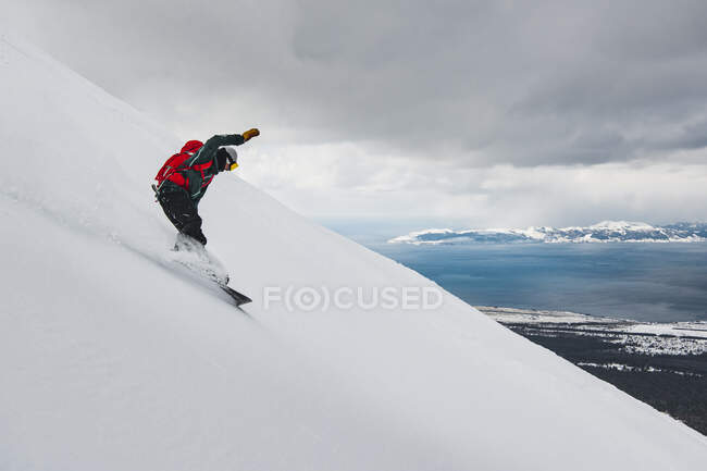 Uomo snowboard su montagna innevata contro cielo nuvoloso durante le vacanze — Foto stock