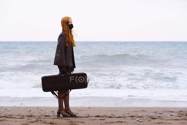 Junge rothaarige Frau mit ihrer Tasche am Strand an einem bewölkten Wintertag — Stockfoto