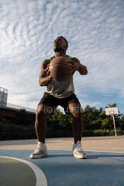 Afro-Américain accroupi et se préparant à lancer le ballon de basket sur le terrain — Photo de stock