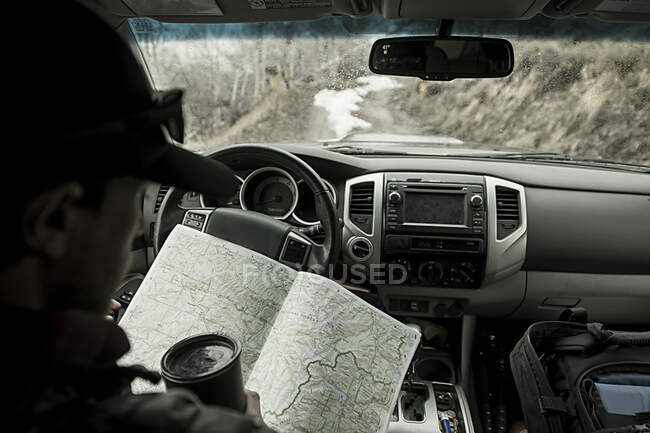 Молодой мужчина смотрит на карту в грузовике во время езды назад дороги Колорад — стоковое фото