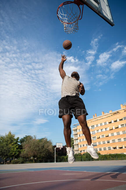 Чернокожий мужчина прыгает и бросает мяч в обруч во время игры в баскетбол на улице — стоковое фото