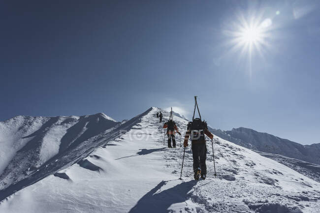 Люди з лижними полюсами під час канікул піднімаються по снігопаду на гору проти неба — стокове фото