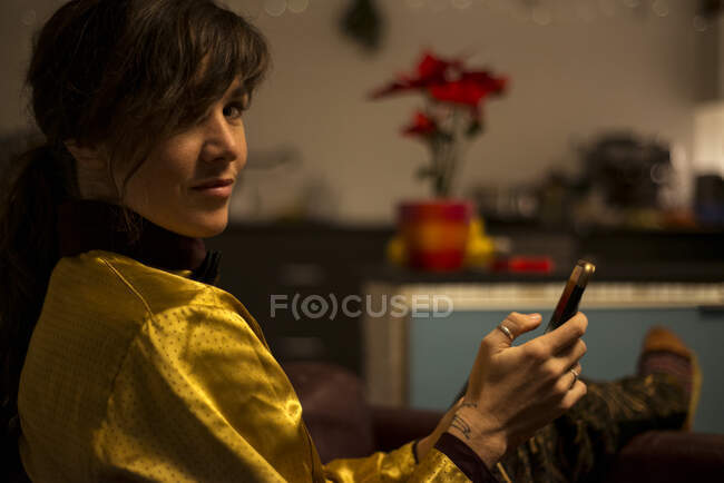 Freckled woman looks to camera whilst typing on phone at home at night — Stock Photo