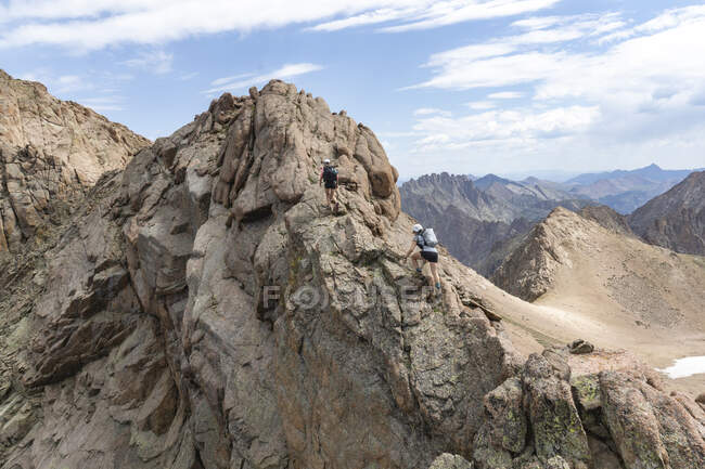 Female friends climbing rocks while hiking on mountain against sky — Stock Photo