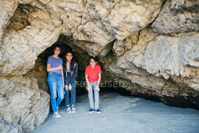 Tres hermanos adolescentes se reúnen dentro de una cueva en la playa - foto de stock